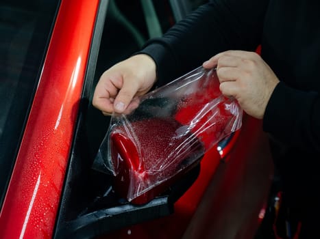 The master applies vinyl film to the side view mirror of a car