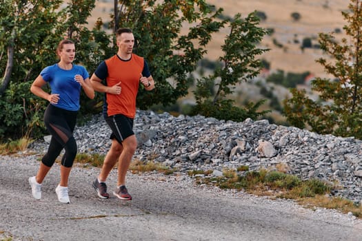 A couple dressed in sportswear runs along a scenic road during an early morning workout, enjoying the fresh air and maintaining a healthy lifestyle.