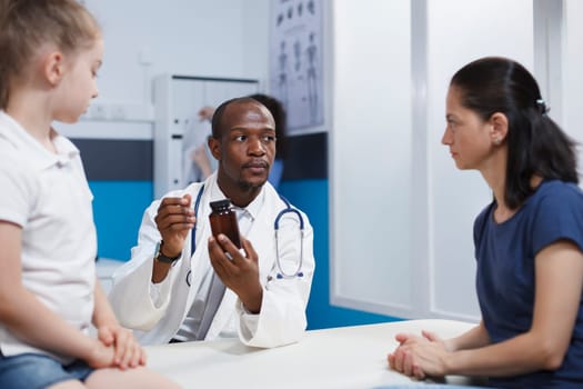 Caucasian mother and daughter intently listening to an African American physician describing the bottle of medicine. They discuss health care with an emphasis on thorough evaluation and treatment.