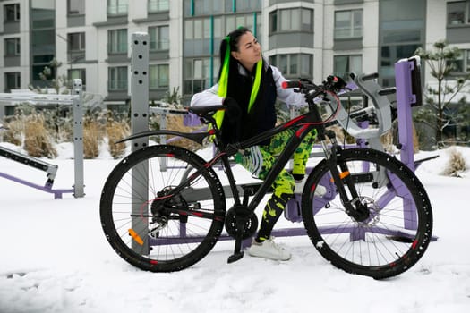 A man, wearing winter clothes, stands next to a bicycle covered in snow. The snow-covered ground indicates cold weather conditions. The man appears to be examining the bike or preparing to ride it in the snowy environment.