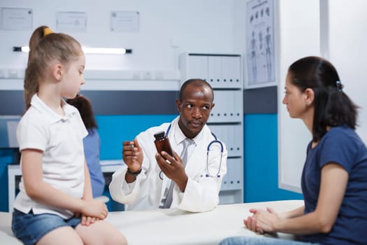 Caucasian mother and daughter speaking with an African American doctor holding a prescription bottle. They talk about health care with a focus on thorough evaluation and treatment.