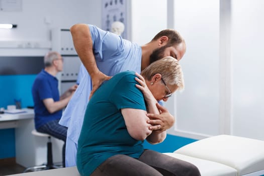 Caucasian senior woman receives checkup from physiotherapist. Patient, recovering from back pain, undergoes spinal pressure examination and engages in rehabilitative exercises with guidance.