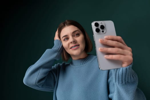 A woman holding a phone up in front of her face, smiling and posing for a selfie. She is using the front camera to capture herself in the moment.