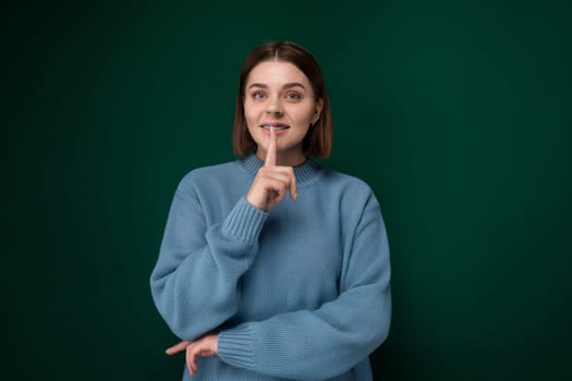 A woman wearing a blue sweater is pointing her finger directly at the camera in a confident gesture. She appears determined and focused on conveying a message or emphasizing a point.