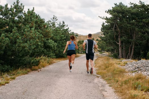 A couple dressed in sportswear runs along a scenic road during an early morning workout, enjoying the fresh air and maintaining a healthy lifestyle.