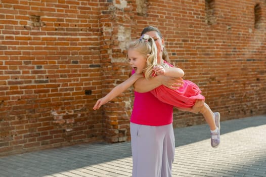 Blonde little girl with cochlear implant playing with her mother outdoor. Hear impairment deaf and health concept. Diversity and inclusion. Copy space.