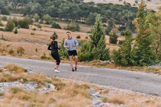 A couple dressed in sportswear runs along a scenic road during an early morning workout, enjoying the fresh air and maintaining a healthy lifestyle.