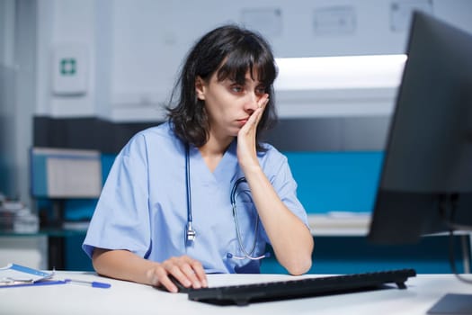 In office, medical assistant uses a computer and mouse for the healthcare system. While working late at night, the nurse is glancing at the monitor screen for support and assistance.