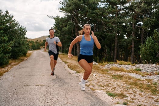 A couple dressed in sportswear runs along a scenic road during an early morning workout, enjoying the fresh air and maintaining a healthy lifestyle.