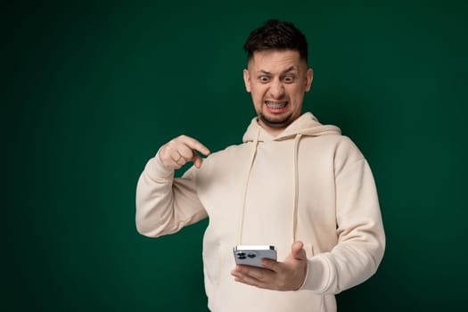 A man wearing a hoodie is holding a cell phone in his hand, looking at the screen. He appears focused and engaged with the device, possibly texting or browsing the internet.