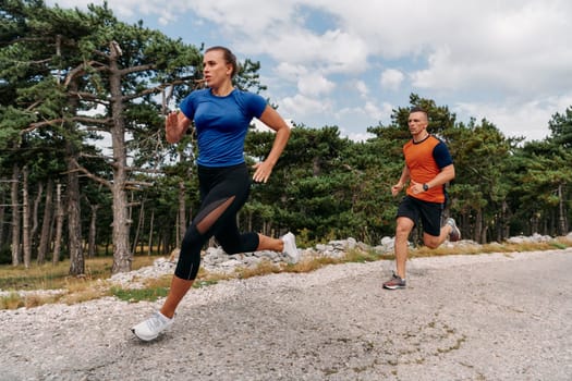 A couple dressed in sportswear runs along a scenic road during an early morning workout, enjoying the fresh air and maintaining a healthy lifestyle.