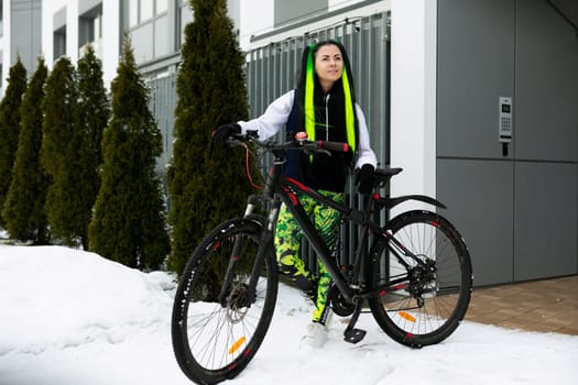 A woman is standing next to a bicycle in a snowy landscape. She is dressed warmly and appears to be taking a break from riding her bike in the winter weather.