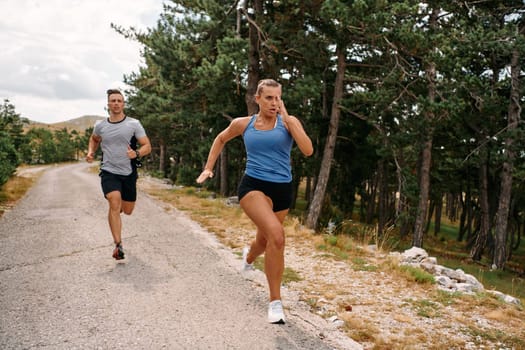 A couple dressed in sportswear runs along a scenic road during an early morning workout, enjoying the fresh air and maintaining a healthy lifestyle.