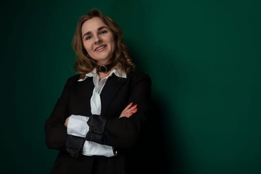 A woman stands with her arms crossed in front of a vibrant green wall. She appears confident and assertive in her posture. The setting showcases a modern and clean environment.