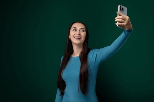 A woman is holding a cell phone and taking a picture of herself. She is seen smiling at the phones screen as she captures the selfie.