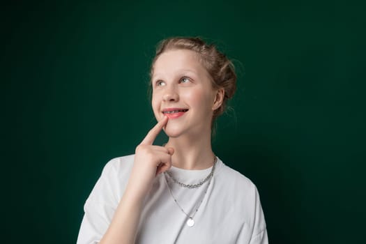 A woman is standing in a pose, placing her index finger on her lips. She is looking directly at the camera, with a slight smile on her face.