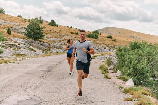 A couple dressed in sportswear runs along a scenic road during an early morning workout, enjoying the fresh air and maintaining a healthy lifestyle.