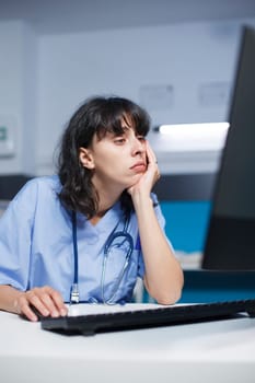 Caucasian female practitioner at a modern clinic desk, tired but focused. Before an appointment, pharmacist trained nurse analyzes a medical checkup using computer in the hospital office.