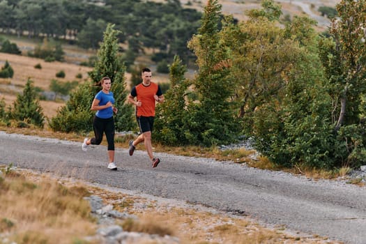 A couple dressed in sportswear runs along a scenic road during an early morning workout, enjoying the fresh air and maintaining a healthy lifestyle.