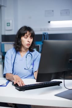 At the clinic office desk, a determined Caucasian nurse checks and analyzes her notes. Close-up shot of physician in blue scrubs getting ready to see people for medical consultations.
