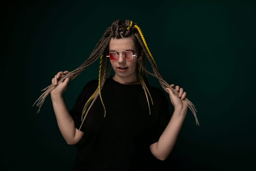 A man with long, thick dreadlocks and red glasses is standing outdoors. He has a confident expression on his face and appears to be looking at something in the distance.