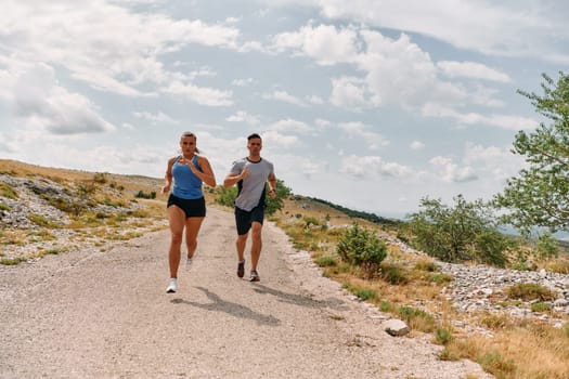 A couple dressed in sportswear runs along a scenic road during an early morning workout, enjoying the fresh air and maintaining a healthy lifestyle.