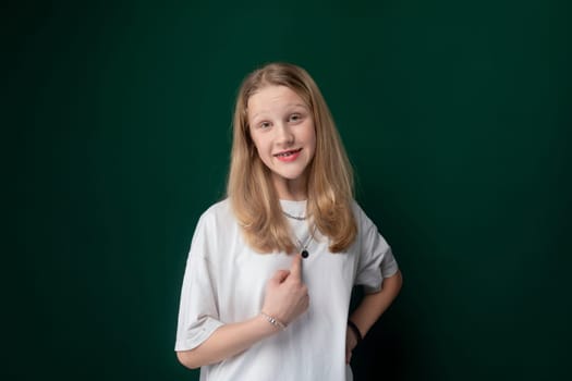 A woman is standing in front of a solid green wall, looking directly at the camera with a neutral expression. She is wearing casual clothing and appears to be stationary.