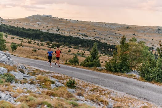 A couple dressed in sportswear runs along a scenic road during an early morning workout, enjoying the fresh air and maintaining a healthy lifestyle.