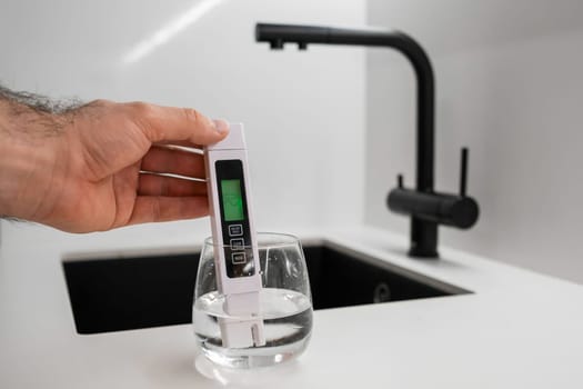Man hand immerses TDS tester or conductometer into the water in glass. demonstrates that the water is clean.