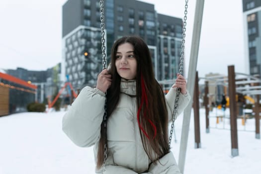 A woman is seated on a swing in a snowy landscape. She is bundled up in winter attire, with snow covering the ground around her. The swing is gently swaying back and forth as she enjoys the peaceful scene.