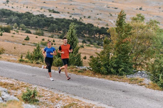 A couple dressed in sportswear runs along a scenic road during an early morning workout, enjoying the fresh air and maintaining a healthy lifestyle.