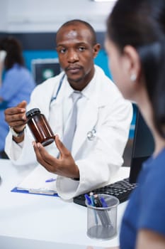 Close-up of an African American doctor explaining diagnosis and treatment to the Caucasian woman while holding a bottle of medicine. Female patient receiving health care consultation.