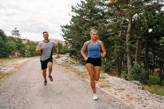 A couple dressed in sportswear runs along a scenic road during an early morning workout, enjoying the fresh air and maintaining a healthy lifestyle.