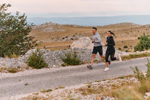 A couple dressed in sportswear runs along a scenic road during an early morning workout, enjoying the fresh air and maintaining a healthy lifestyle.