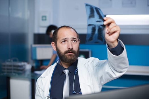 Selective focus of a caucasian doctor holding and examining a chest X-ray image of a patient. Close-up shot of a male physician grasping and studying a chest scan of an individual.