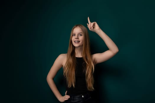 A young woman is standing in front of a vibrant green wall while posing for a picture. She is looking directly at the camera with a confident expression, her arms relaxed by her sides.