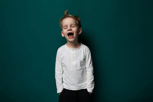 A young boy with his eyes closed standing in front of a vibrant green wall, showcasing a moment of reflection or concentration. His body language suggests a sense of stillness and contemplation.