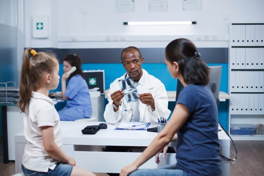 During doctor appointment in hospital office, an African American pediatrician doctor reviews a child radiograph of the lungs and discusses the child's illness symptoms with the mother.