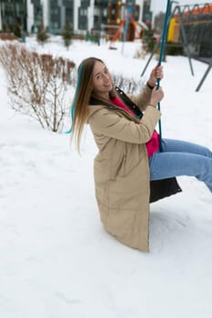 A woman is seated on a swing that is covered in snow. She appears relaxed, enjoying the winter scenery around her.