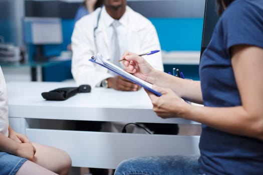 Close-up image of a caucasian woman in the hospital filling out papers for a medical checkup with African American doctor. This appointment provides high-quality treatment and guidance.