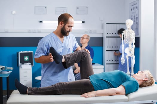 Physiotherapist stretching leg muscle to relieve pressure for recovery of senior woman. Doctor assistant helping aged patient with knee pain, doing physical exercise for physical therapy.