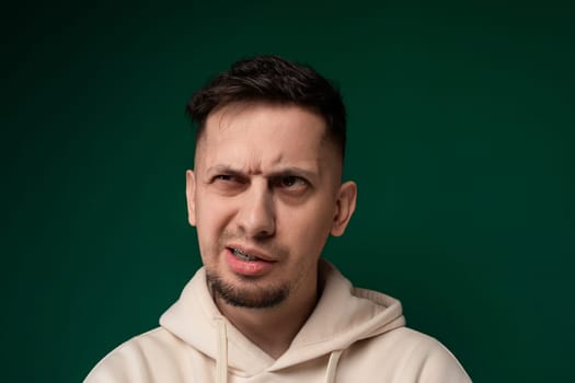 A man wearing a hoodie is contorting his face, showcasing various expressions such as grimacing, wincing, and squinting. His facial features are highlighted by the hoodies shadow.