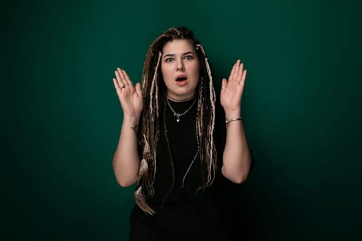 A woman with dreadlocks is posed in front of a vibrant green background. She is standing upright, looking directly at the camera with a composed expression.