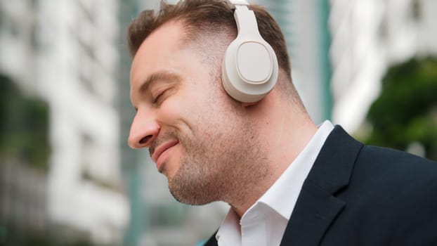 Close up of businessman listen headphone and dancing to relaxing music with cheerful and motivation. Skilled project manager enjoy to listen relaxed song with blurred background at urban city. Urbane.
