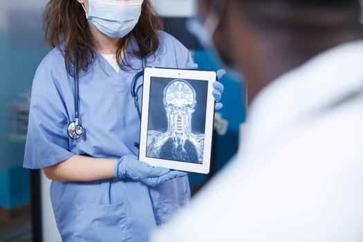 Doctor analyzes medical results for patients in an office. Examining the findings using a digital tablet and a screen displaying a skull scan. Scene conveys professionalism and expertise in neurology.