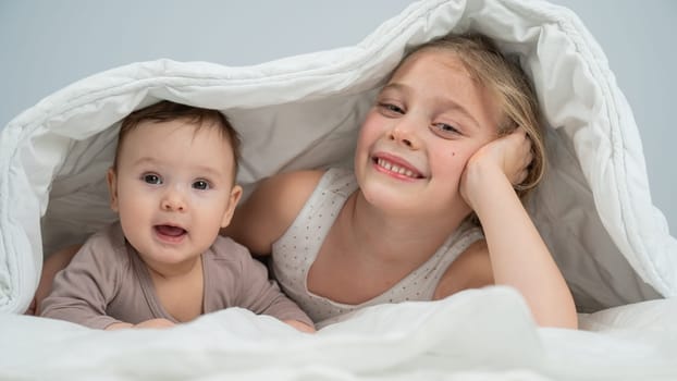 Little girl and her newborn brother hiding under the blanket