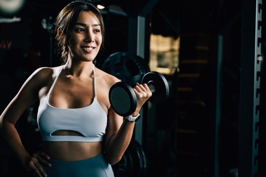 An Asian woman with a slim and fit body, holding a weight and smiling, showcases her dedication to fitness and health through exercise and weightlifting.