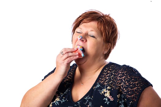 Overweight fifty something woman stuffing a cupcake in her mouth