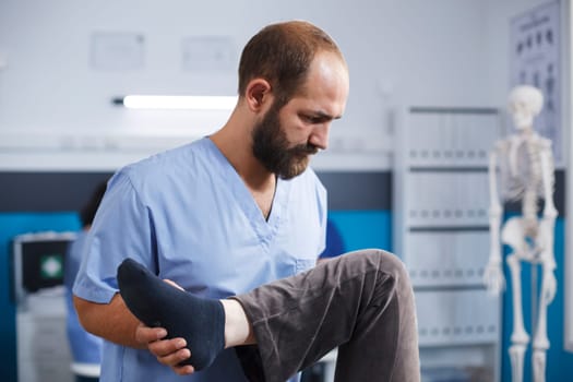 Close-up of chiropractor providing assistance to elderly patient with knee injury for physical recovery. Senior person doing leg exercise with help from medical assistant for osteopathic remedy.