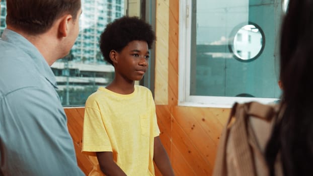 Smiling african boy sitting in circle while listening diverse friend sharing idea in group therapy with trust. Highschool student thinking and learning about mental health problem. Edification.